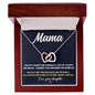 An Interlocking Hearts Necklace with cubic zirconia crystals, displayed in front of a wooden box with a card that reads 'Mama' and a message from a daughter.