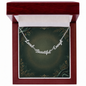 A silver script affirmation nameplate necklace reading 'Loved Beautiful Enough' displayed inside an open dark red wooden gift box with a green insert card.