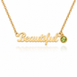 A gold affirmation necklace spelling 'Beautiful' in cursive script, with a small round green gemstone accent on the right side, shown on a clean white background with a soft reflection.