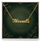 Gold script affirmation necklace spelling 'Blessed' with a small round amber gemstone pendant, displayed on a dark green decorative presentation card inside a white box.