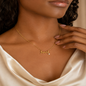 A close-up of a model wearing a delicate gold script necklace with the word 'love' and a small pearl accent, paired with a cream satin top.