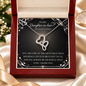 A silver heart-shaped pendant necklace displayed inside an open red gift box on a printed message card addressed to a daughter-in-law. The necklace has a double-heart design with small clear stones.