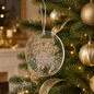 A round clear acrylic Christmas ornament hanging from a silver string on a decorated Christmas tree. The ornament features the words 'Season's Greetings' in elegant gold script, a printed holiday poem, and illustrations of pinecones, pine needles, and berries.