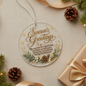 Round hanging ornament with 'Season's Greetings' in gold script and a holiday verse, styled on a beige fabric surface with pine branches, ribbon, string lights, and a wrapped gift box.