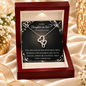 A silver double-heart necklace displayed inside an open dark red gift box with a message card addressed to a daughter-in-law, set on draped satin fabric with decorative flowers and ribbons.