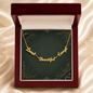 A gold script affirmation necklace spelling out 'Loved Beautiful Enough' rests on a dark green velvet jewelry card inside an open dark red wooden gift box. The box is set against a soft beige satin fabric background.