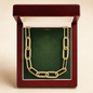 A gold chain necklace with diamond-encrusted links displayed inside an open dark red wooden jewelry box with a green insert, set against a light beige background.